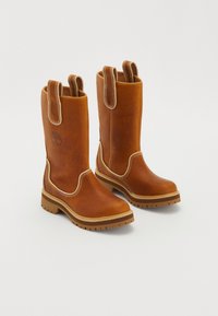 Pari ruskeih nahkastih čizm do kolen s povlekami, bežnim šivom, debelim gumijastim podplatom in embosiranim logotipom drevesa na zunanji strani.