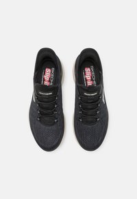 Black athletic slip-on shoes with mesh upper, elastic laces, and a cushioned sole. Brand logos visible on the tongue and side.