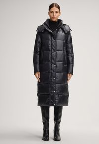 Czarna pikowana kurtka puchowa o długim kroju, duży kaptur, zapięcie na zatrzaski i boczne kieszenie. Noszona z czarnymi, sięgającymi kolan kozakami.