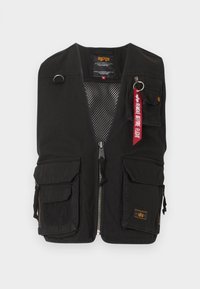 Μαύρο χρηστικό γιλέκο με πολλαπλές μπροστινές τσέπες, κλείσιμο με φερμουάρ, εσωτερική επένδυση από δίχτυ και κόκκινο μπρελόκ με την επιγραφή "Remove Before Flight" στην πάνω δεξιά τσέπη.