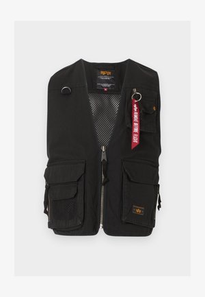 Black utility vest with multiple front pockets, zipper closure, mesh inner lining, and red "Remove Before Flight" keychain on top right pocket.