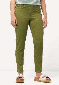 Vihreät puuvillahousut, joissa on slim fit ja viisi taskua. Yhdistettynä valkoisiin sandaaleihin, joissa on puinen kantapää ja solk yksityiskohta.