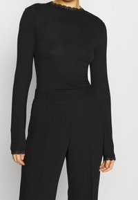 Svart långärmad topp med en passande design, spetsdetaljer vid halsringningen och ärmarna, slät textur och en enkel silhuett.