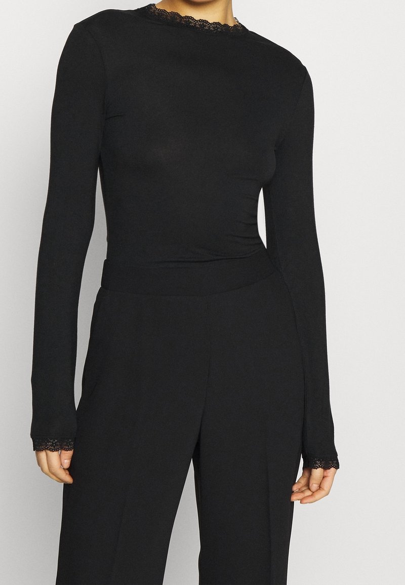 Svart långärmad topp med en passande design, spetsdetaljer vid halsringningen och ärmarna, slät textur och en enkel silhuett.