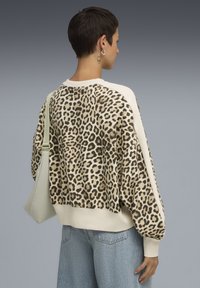 Sweatshirt à imprimé léopard avec une coupe décontractée, manches crème et poignets côtelés, associé à un jean taille haute bleu clair.