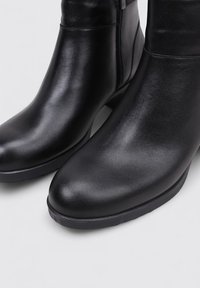Par de botas de cuero negras hasta el tobillo con punteras redondeadas y cremalleras laterales sobre un fondo claro.