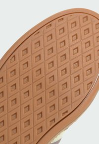 Gumowa podeszwa buta o teksturowanej, beżowej powierzchni z wzorem w kratkę. Krawędzie są gładkie, a materiał wydaje się wytrzymały i elastyczny.