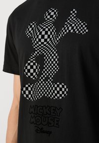 Camiseta negra con un gráfico de Mickey Mouse de cuadros en blanco y negro, con el texto "MICKEY MOUSE" y "Disney" debajo.