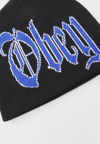 Black knitted beanie featuring blue and white embroidered gothic-style text. Smooth texture with a snug fit.