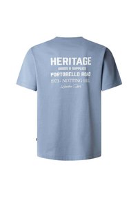 Light blue cotton t-shirt with short sleeves. Back features white printed text reading "HERITAGE," "PORTOBELLO ROAD 1973 - NOTTING HILL," and "London W."
