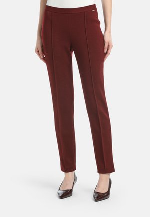 Maroon tailored pants with a smooth texture, featuring two front creases, a mid-rise waistband, and side pockets. Worn with pointed-toe heels.
