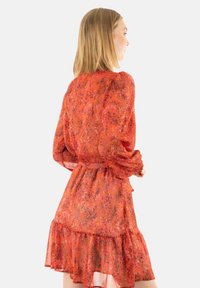 Vestido rojo de flores con tejido transparente, mangas largas abullonadas, dobladillo con volantes y cintura ajustada. Presenta un patrón vibrante y una textura ligera.