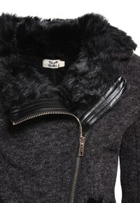 Chaqueta negra con cremallera, que presenta un cuello de piel sintética, tejido texturizado y detalles lisos en negro en los hombros, con un detalle de cremallera visible.