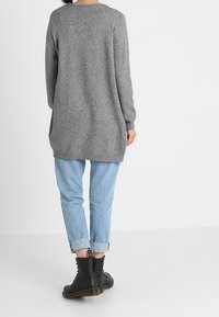 Szary sweter z długim rękawem o luźnym kroju, zestawiony z jasnoniebieskimi jeansami z podwiniętymi mankietami i czarnymi botkami, prezentujący swobodny wygląd.