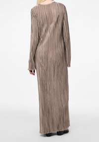 Robe longue à côtes dans une couleur taupe douce, avec des manches longues et un col rond. Le tissu a une finition lisse et texturée.