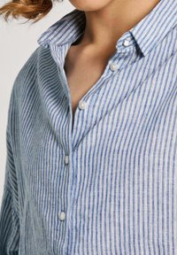 Light blue and white striped shirt made of textured fabric, featuring a pointed collar and button placket with round buttons.