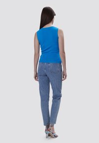 Top sin mangas azul combinado con jeans de rayas azules claros, con un corte a media altura y puños acampanados, complementado por tacones azul claros.