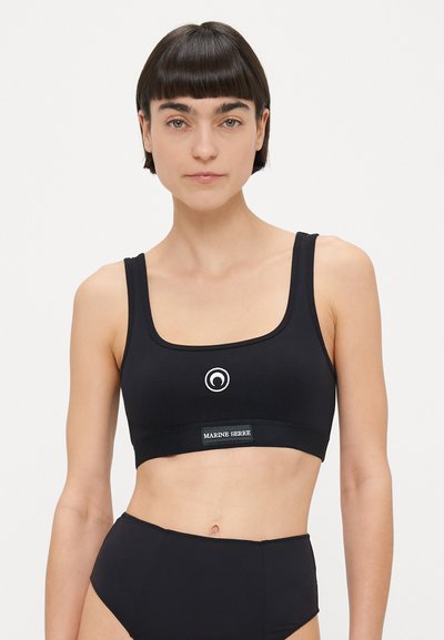 Haut court noir avec encolure carrée, larges bretelles et un logo circulaire sur le devant. Le matériau semble lisse avec une coupe ajustée.