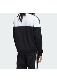 Svart och vit sweatshirt med en färgblockdesign, tillverkad av mjukt tyg, med långa ärmar och ribbade muddar. Tre vertikala ränder på ärmarna.