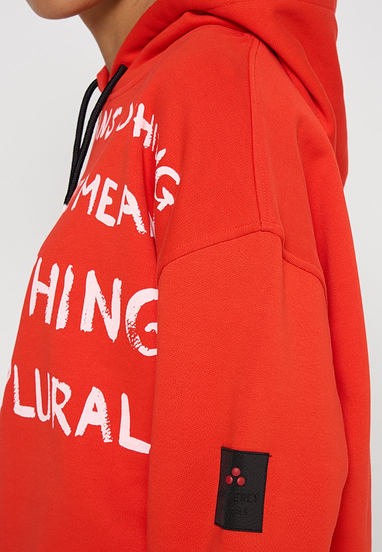 Czerwona hoodie z białym tekstem i grafikami z przodu, z czarną metką na rękawie. Miękka struktura i regulowany kaptur ze sznureczkiem.