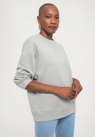 Hallide hall sweatshirt, kusete varrukatega, ümmarguse kaelusega ja soonikserva ääristusega. Materjal näib pehme ja kerge tekstuuriga. Kandmisele on koos helesiniste teksadega.