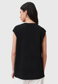 Schwarzes Baumwoll-T-Shirt mit kurzen, aufgerollten Ärmeln, einem runden Halsausschnitt und einer lockeren Passform, von hinten betrachtet. Glatte Textur.