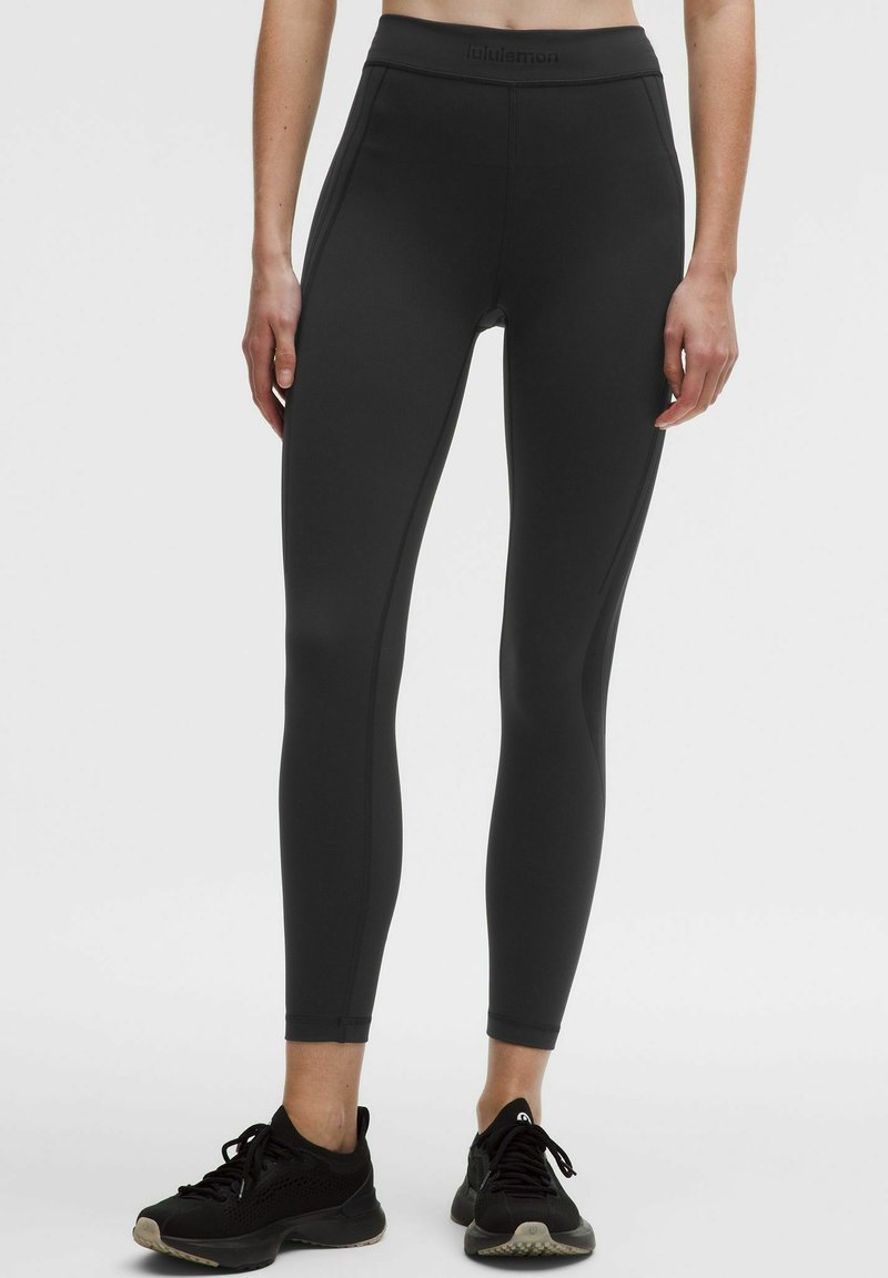 Črne legice z visokim pasom iz raztegljive tkanine, z nešitim pasom in šivi ob straneh, zasnovane za prožnost.