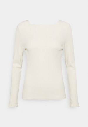 Top de mujer de manga larga en color crema con escote cuadrado y puños sutilmente fruncidos sobre un fondo blanco liso.