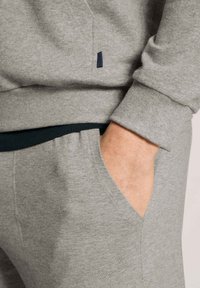 Grijs sweatshirtmateriaal met geribbelde manchetten en een zak. Heeft een kleine blauwe accent nabij de naad. Zachte textuur, casual ontwerp.