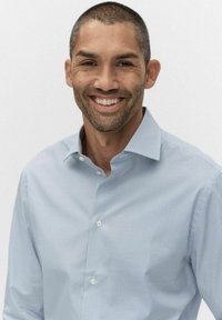 Lysblå skjorte med knapper og geometrisk mønster, udstyret med spredt krave og hvide knapper, båret af en smilende mand.