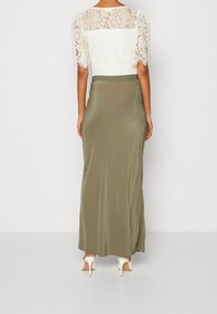 Maxiklänning med en vit spetsöverdel och en olivgrön satinnedlängd. Har puffärmar och en slät, svävande design. Över-knee fåll bak.