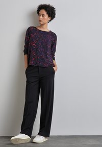 Zwarte, losse broeken gecombineerd met een langemouwen top met een veelkleurig bloemenpatroon. Witte sneakers maken de outfit compleet.