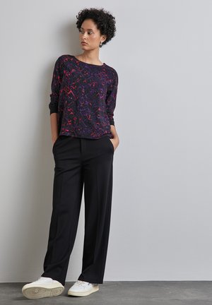 Un pantalon noir ample associé à un haut à manches longues avec un motif floral multicolore. Des baskets blanches complètent la tenue.
