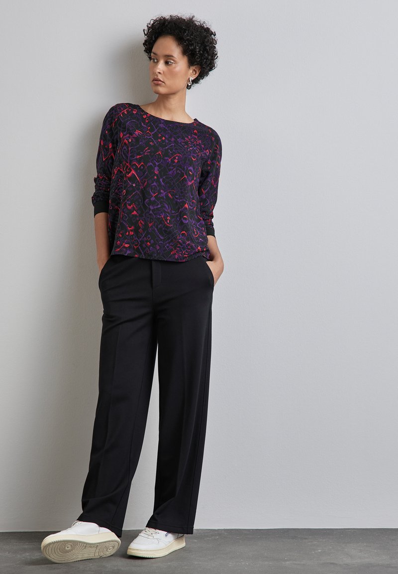 Zwarte, losse broeken gecombineerd met een langemouwen top met een veelkleurig bloemenpatroon. Witte sneakers maken de outfit compleet.