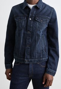 Chaqueta vaquera azul oscuro con cierre de botones, bolsillos en el pecho y bolsillos laterales. Diseño clásico con costuras en contraste y un ajuste estructurado.