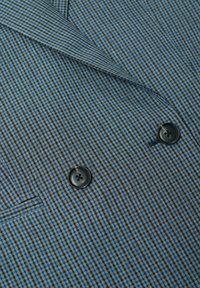 Tissu à motif pied-de-poule bleu et noir avec une texture lisse, comportant deux boutons noirs sur une veste de costume ajustée.