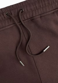 Bruine sweatpants met een elastische tailleband en trekkoord. Gladde textuur met een metalen accent aan het einde van het trekkoord.