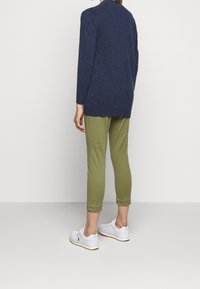 Suéter de manga larga en navy combinado con pantalones cortos verde oliva y zapatillas blancas, con un ajuste relajado y un diseño simple.