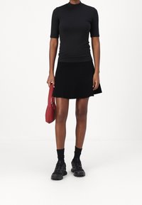 Top negro de manga corta combinado con una falda mini de rayas negras. Sosteniendo un bolso rojo. Zapatos negros con diseño texturizado y calcetines.