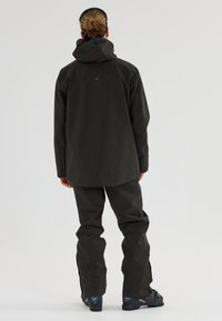 Wasserdichte schwarze Jacke mit Kapuze, kombiniert mit passenden schwarzen Hosen, zeichnet sich durch eine glatte Textur und ein minimalistisches Design aus und eignet sich hervorragend für den Outdoor-Einsatz.