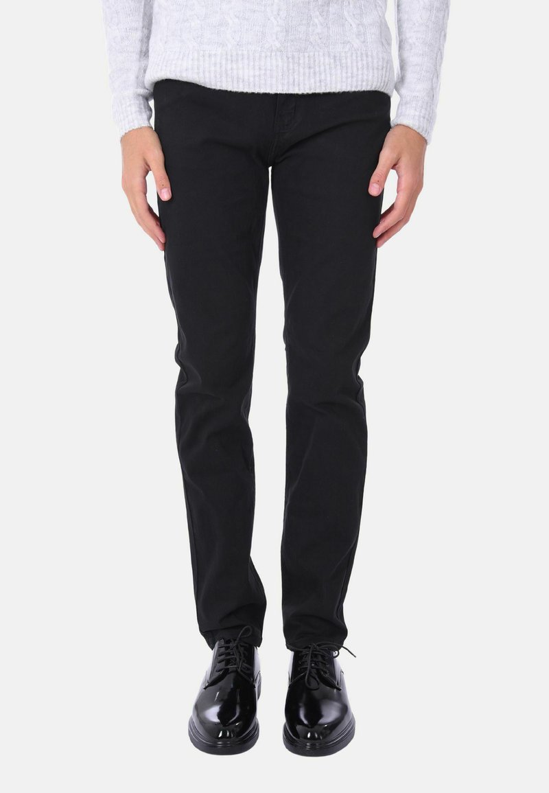 Jeans neri in cotone con vestibilità dritta, abbinati a scarpe eleganti nere lucide e un maglione grigio chiaro a trecce.