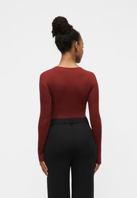 Μακρυμάνικη μπλούζα σε μπορντό με εφαρμοστή γραμμή, συνδυασμένη με ψηλόμεσο μαύρο παντελόνι. Ομαλή υφή με στρογγυλή λαιμόκοψη.