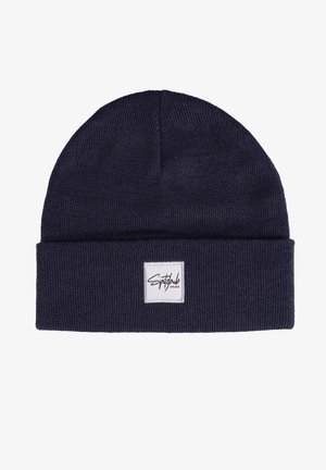 Marineblaue Strickmütze mit umgeschlagenem Bund, ausgestattet mit einem weißen quadratischen Etikett mit schwarzem Text auf der Vorderseite. Weiche Textur, flexibles Material.
