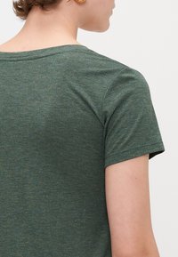 Grøn kortærmet t-shirt lavet af et tekstureret materiale, med en rund halsudskæring og subtile prikker af guldtråd spredt over det.