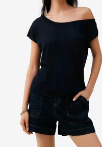Zwarte katoenen t-shirt met korte mouwen, off-shoulder ontwerp, gecombineerd met donkere denim shorts met contrasterende stiksels en zakken.