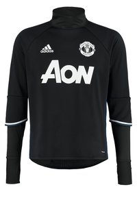 Musta urheilullinen pitkähihainen paita, jossa on korkea kaulus, valkoinen Manchester United -logo, Aon-brändäys sekä erottuvat siniset ja valkoiset yksityiskohdat hihoissa.