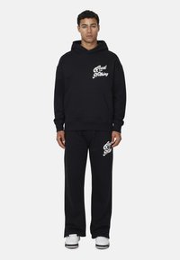 Czarny zestaw bluzy z kapturem i spodni dresowych wykonany z bawełny. Bluza ma kieszeń z przodu i białą tekst na klatce piersiowej. Spodnie dresowe mają pasujący tekst.