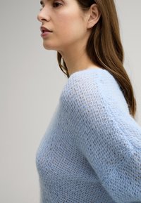 Jasnoniebieski sweter dzianinowy o luźnej, otwartej fakturze. Posiada szeroką linię dekoltu i luźny krój, podkreślający przewiewny design.