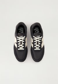 Baskets en mesh noir et en daim avec des accents et des lacets couleur crème, présentant une surface texturée et un design à bout arrondi.