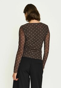 Brun prickig långärmad topp i genomskinligt tyg med en figurnära design, med rund halsringning och veckat bakre detalj.